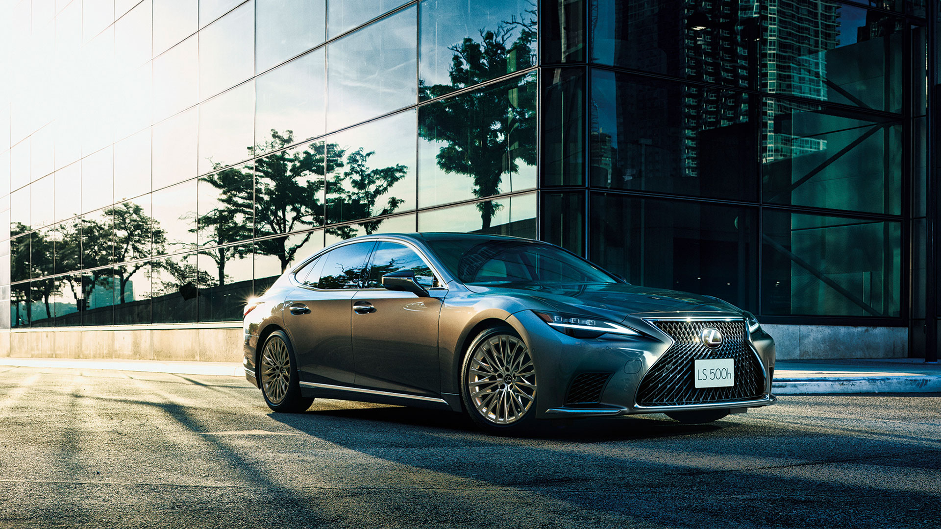 A silver LS parked on a city street next to a glass building.