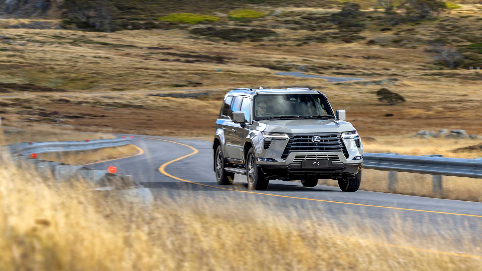 Lexus GX driving on a windy country road with dry grass in the background.