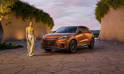 Woman standing next to a car and a tree outside.