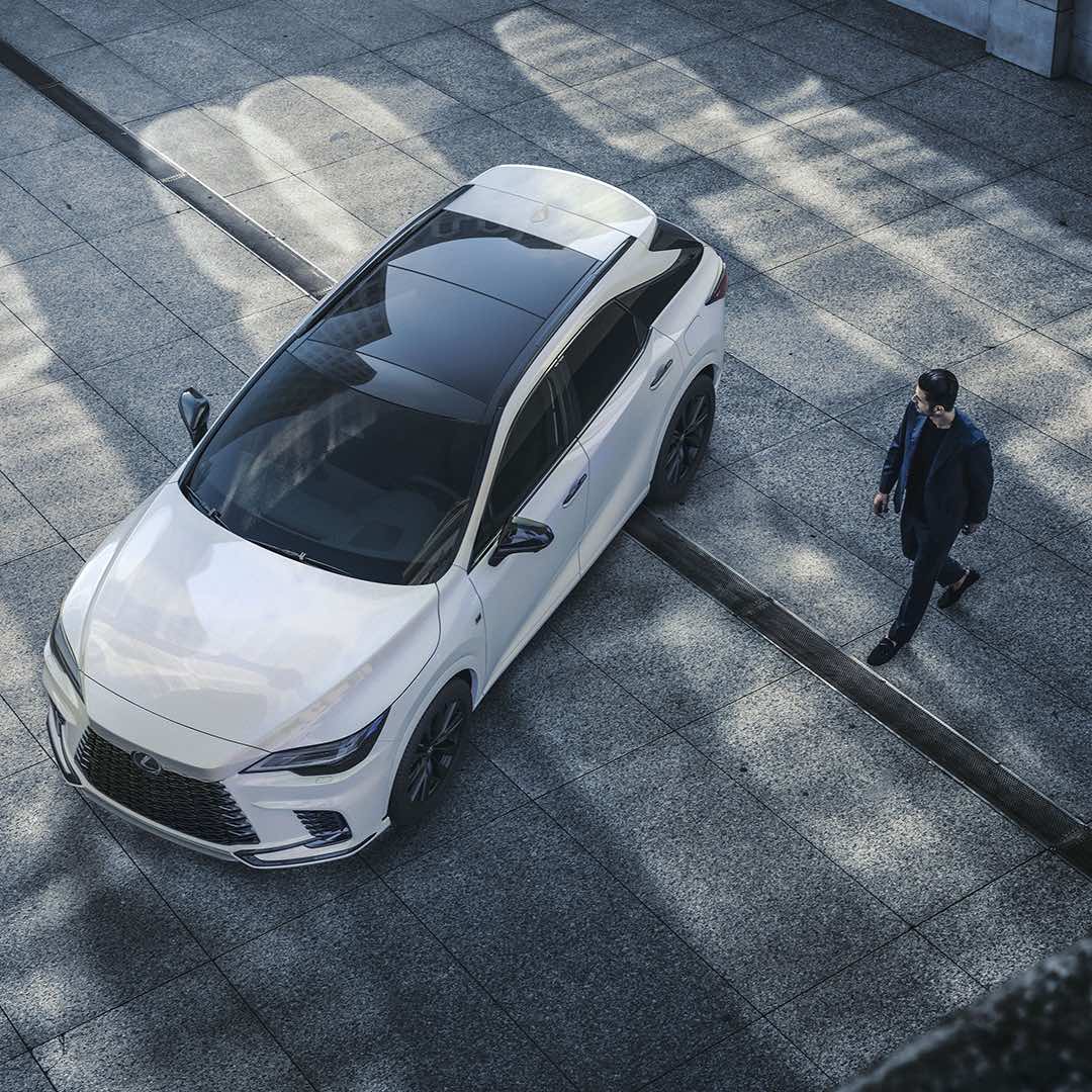 The new RX from above, showing the panoramic roof. The car is parked on a concrete ground, a man is walking towards the car.