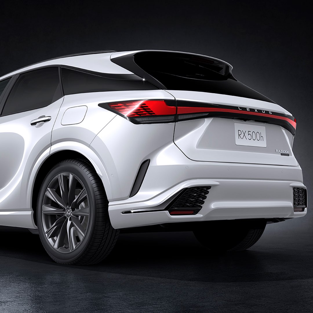 A low shot of the left rear of a white Lexus RX F Sport. The written LEXUS badge and bespoke wheels are featured.