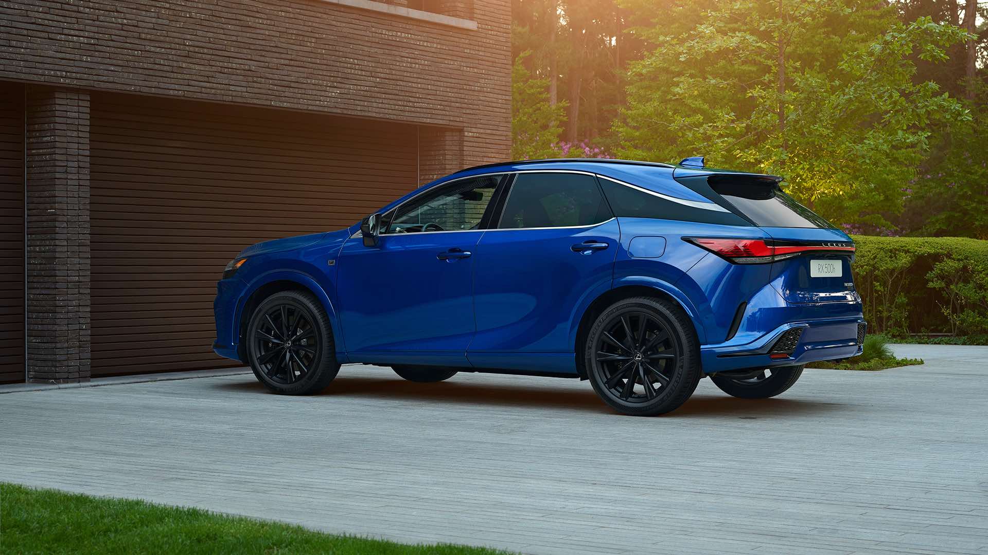 A sapphire blue Lexus RX sits on a concrete driveway. Greenery surrounds it, and a beam of sun brings the top and rear of the vehicle into focus.