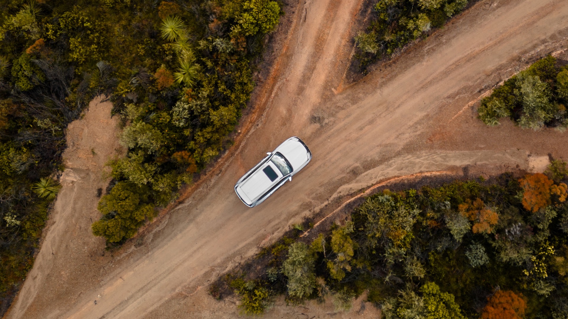 Aerial view of a white Lexus LX driving across dusty roads, which has many forks in it.