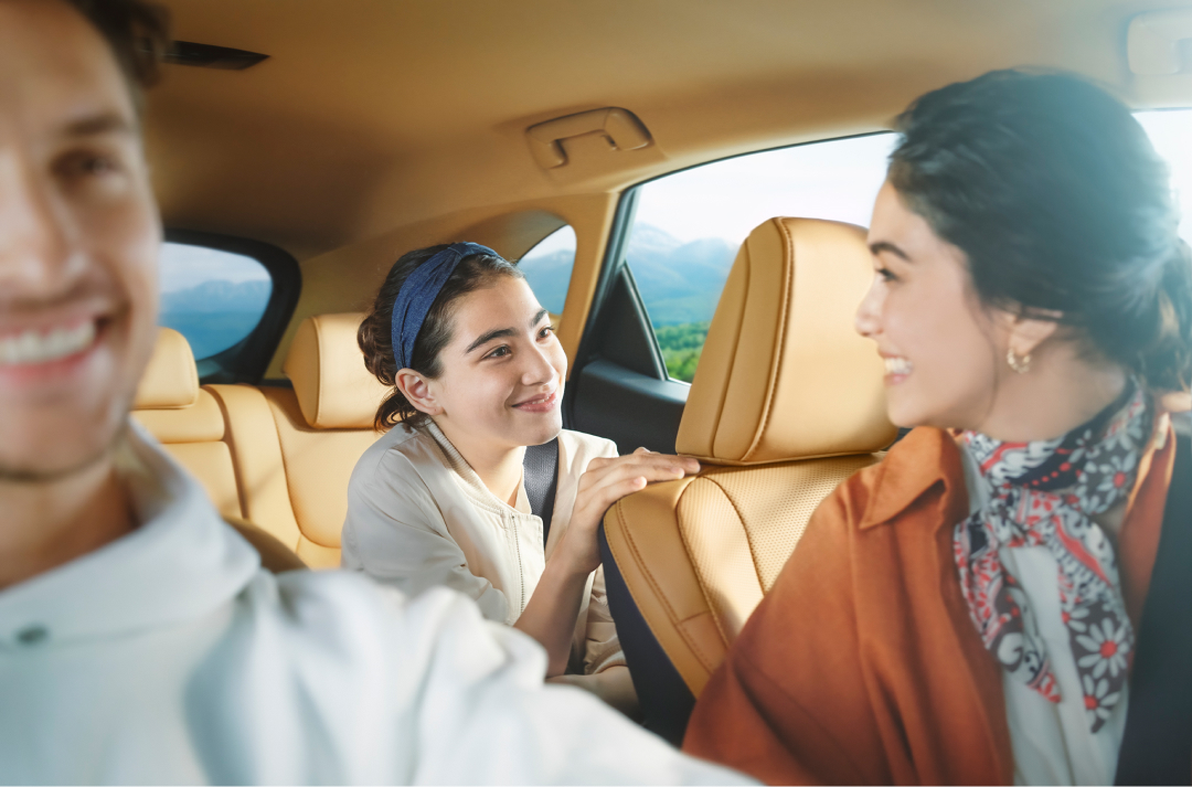 Smiling woman sits in the passenger seat, turning around to a younger girl in the back of a NX