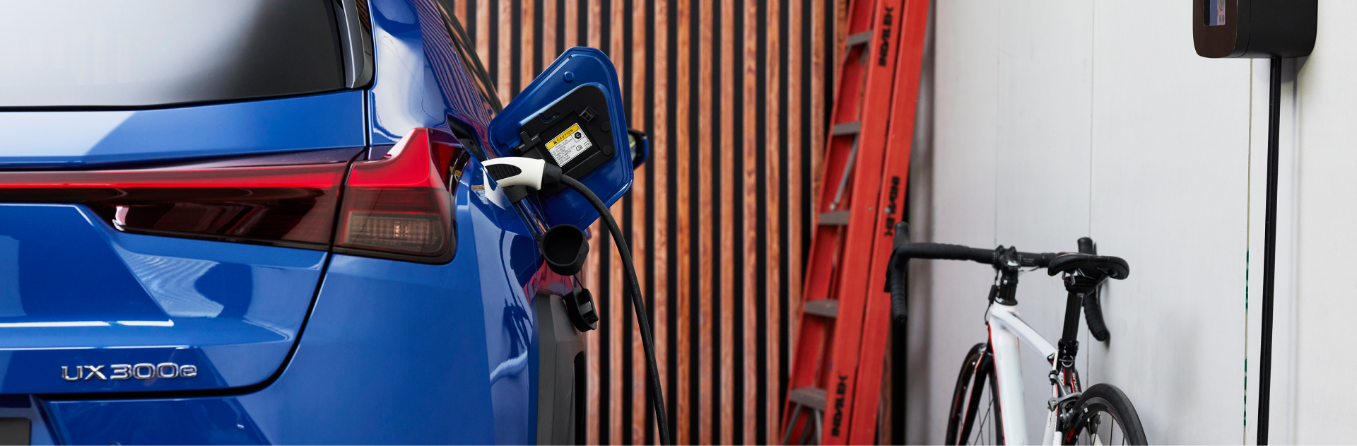 A blue UX 300e charging at home in a garage. A ladder and bike are in the background.