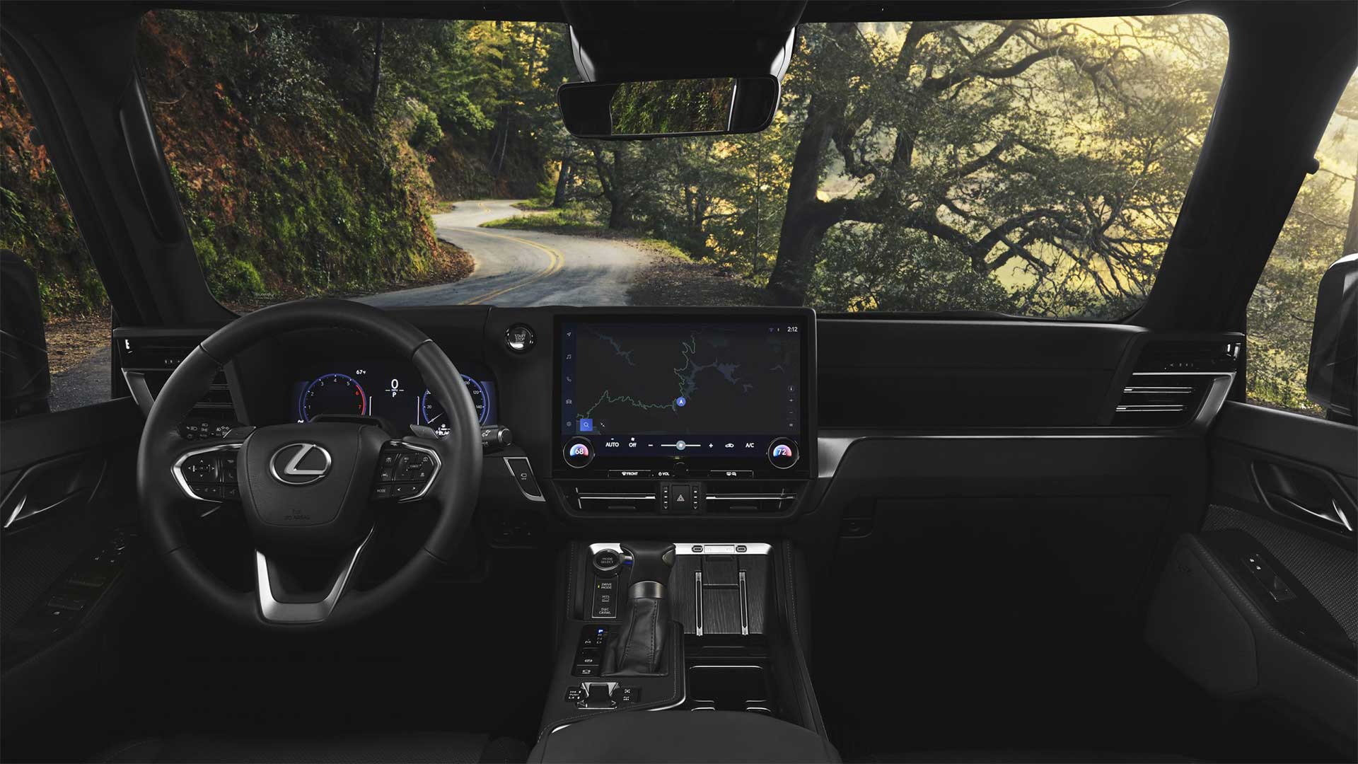 View of the Lexus GX dashboard and steering wheel. Outside is a view of a winding country road with green trees on either side. 