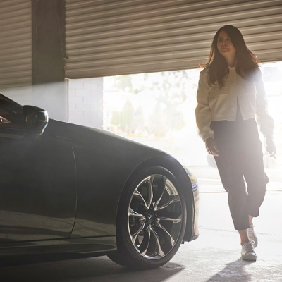 Woman shown walking beside her Lexus LC convertible as a garage door closes behind her.