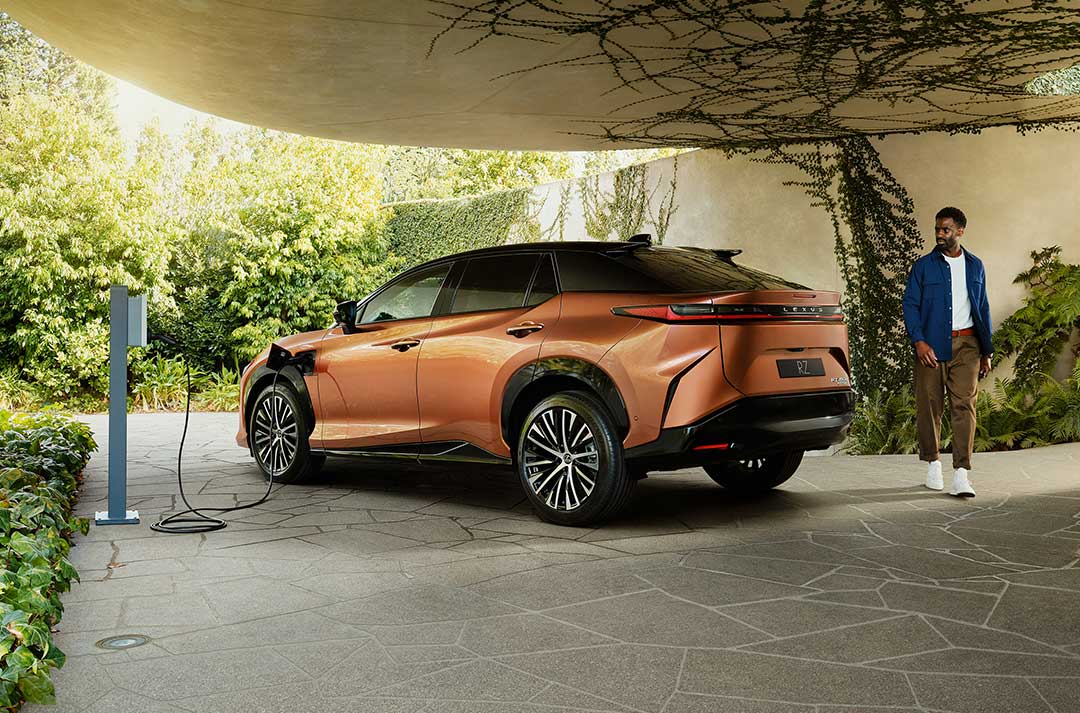 A man walks behind the rear of a charging RZ in a concrete driveway. Vines surround.