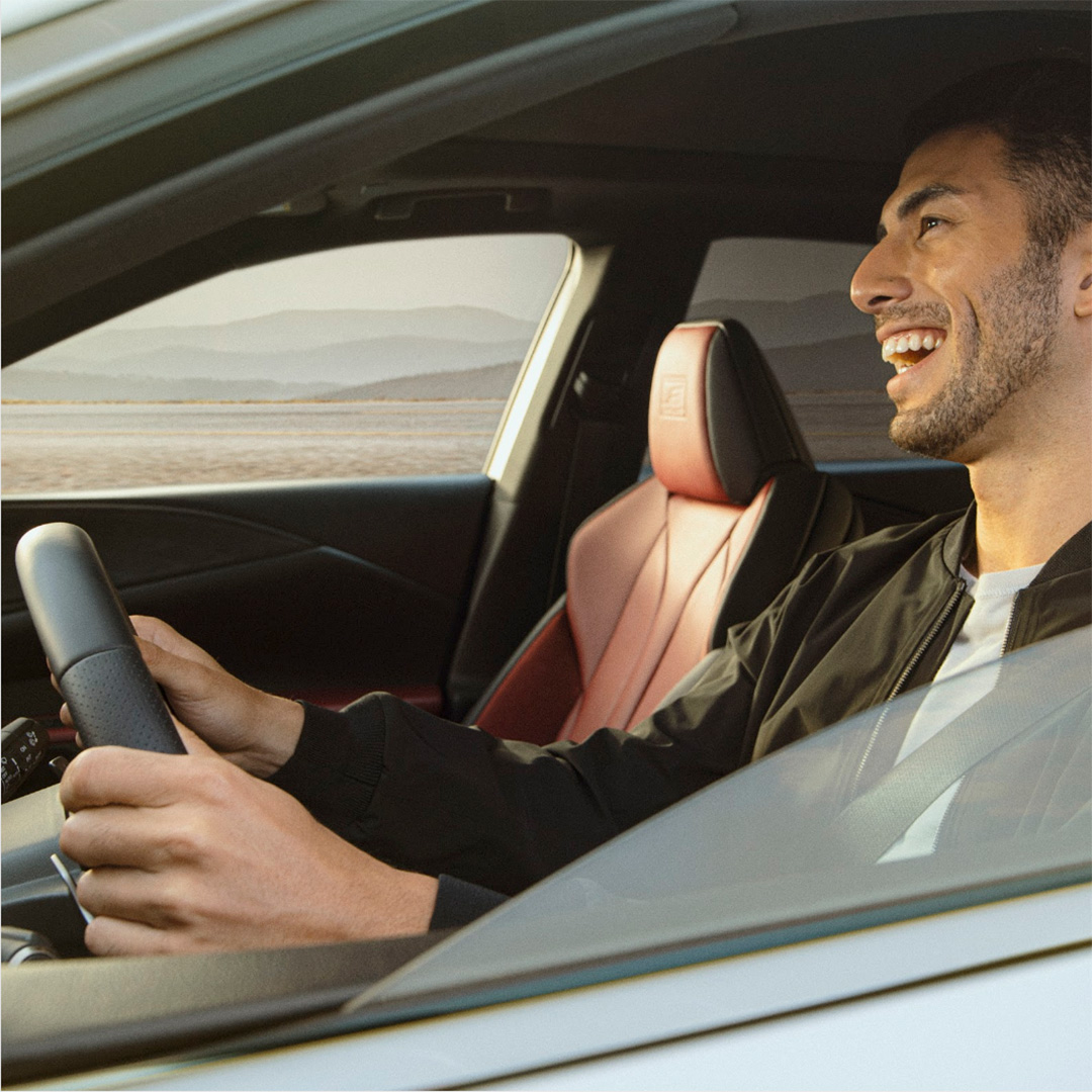 A man drives a non descript car while smiling.
