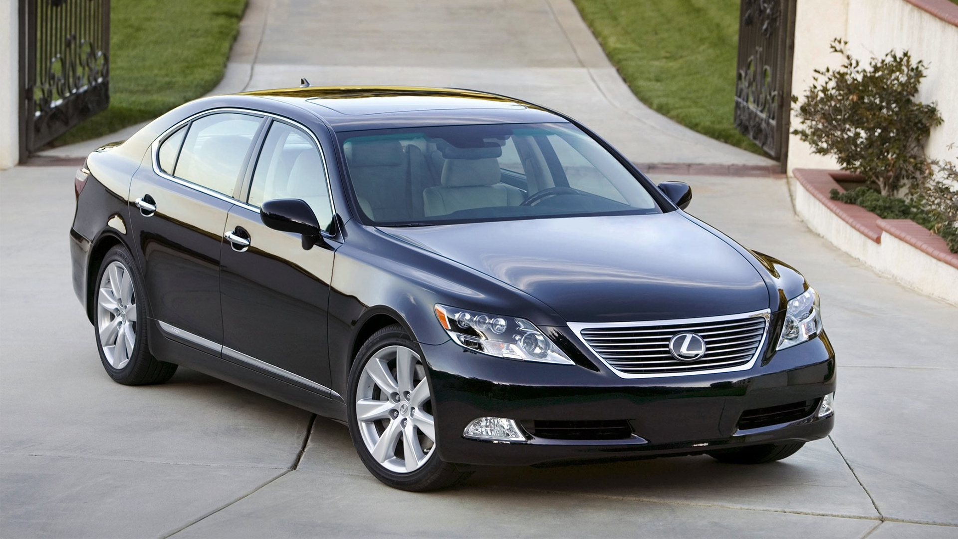 Black Lexus LS 600hL parked on a paved driveway in front of gates.