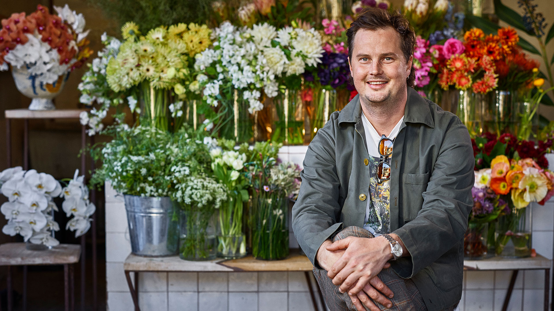 Florist Bryce Heyworth sitting in front of bouquets of flowers