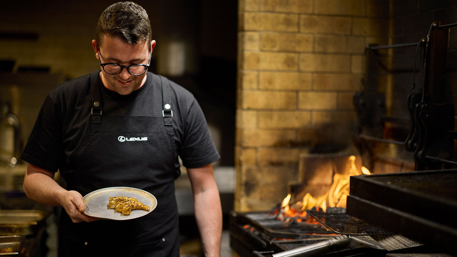 A chef walks in a kitchen with a lamb chop on a plate