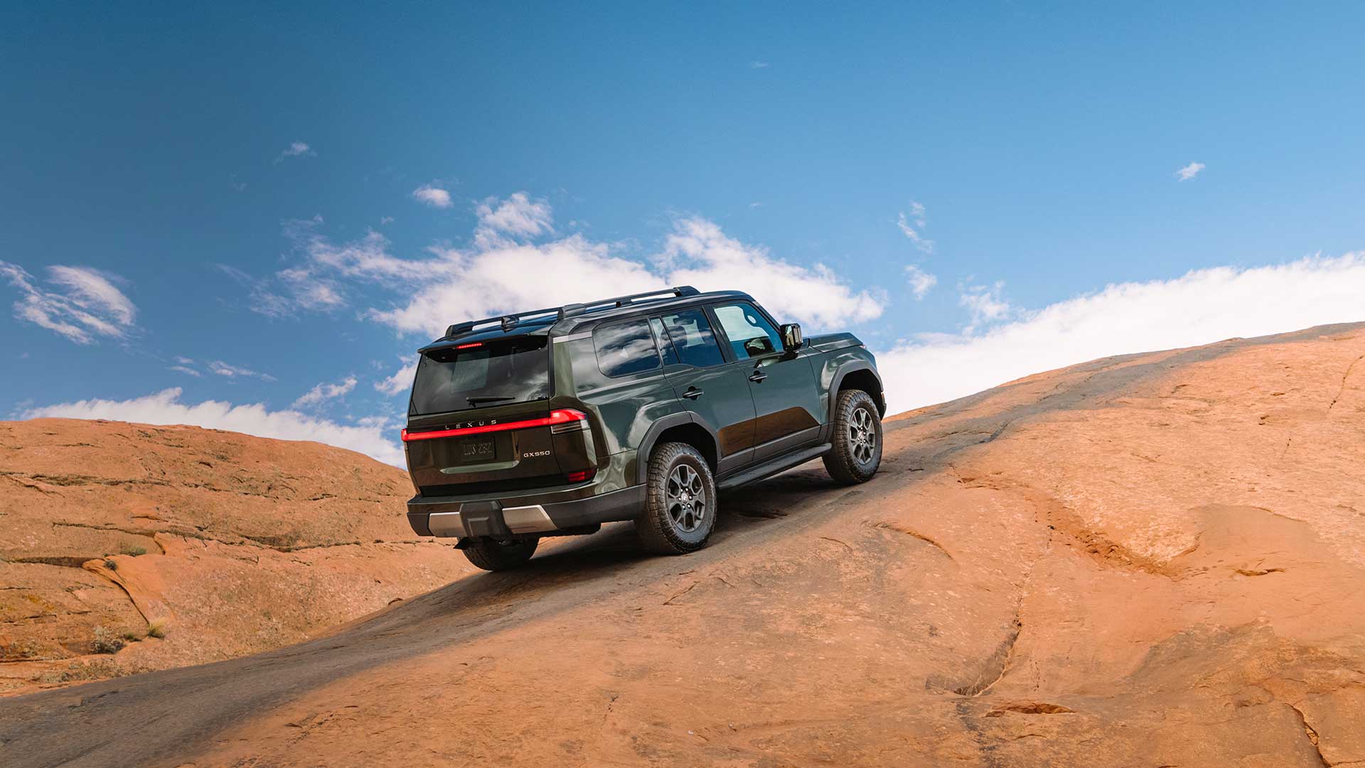 A green Lexus GX driving up a red earth road with a blue sky in the background