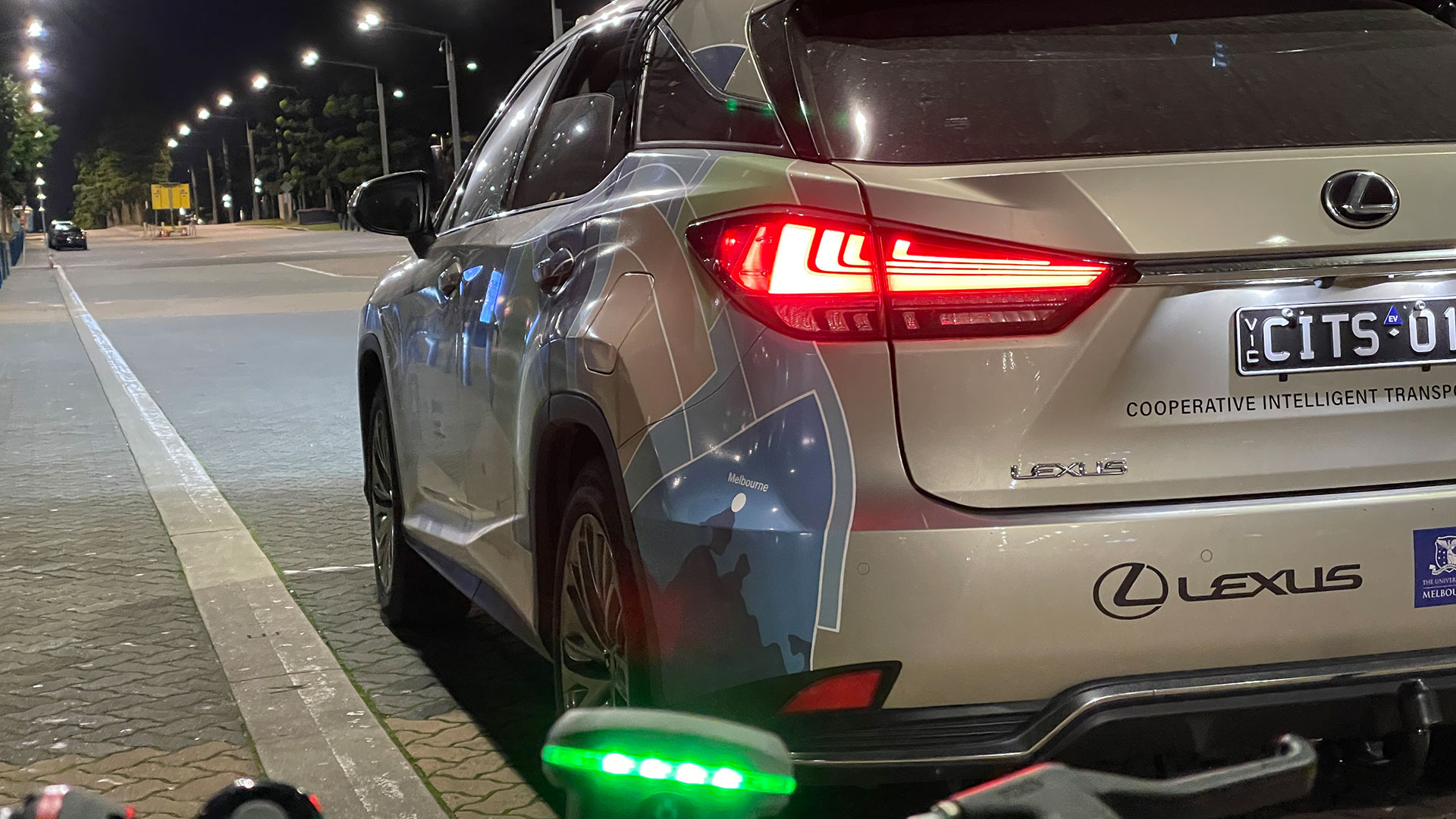 Rear view of silver Lexus SUV with graphic wrap parked along a curb at night