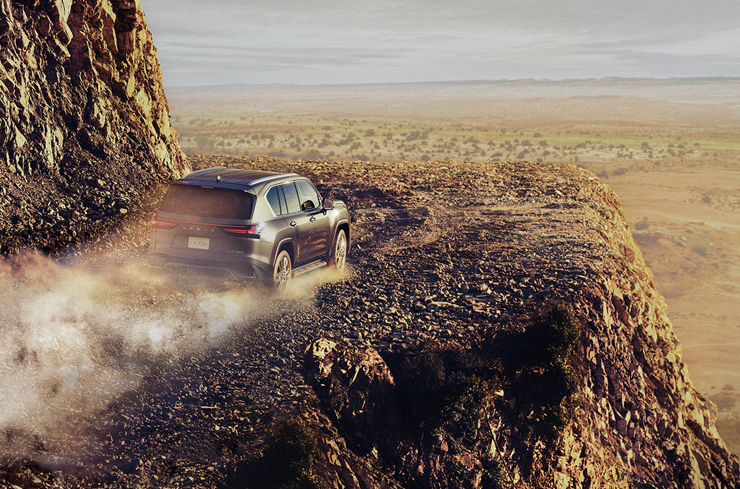 A Lexus LX drives along a rocky road with a desert in the background