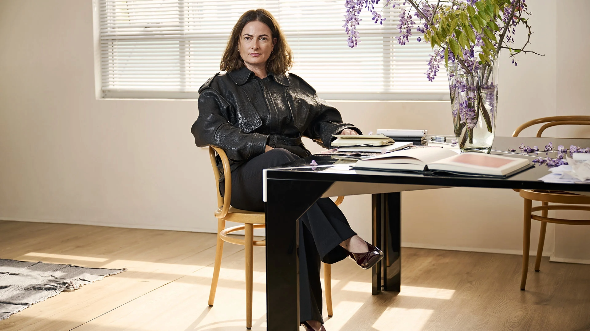 Simone Gooch of Fjura seated at a table with floral arrangements and notebooks in a light-filled studio.